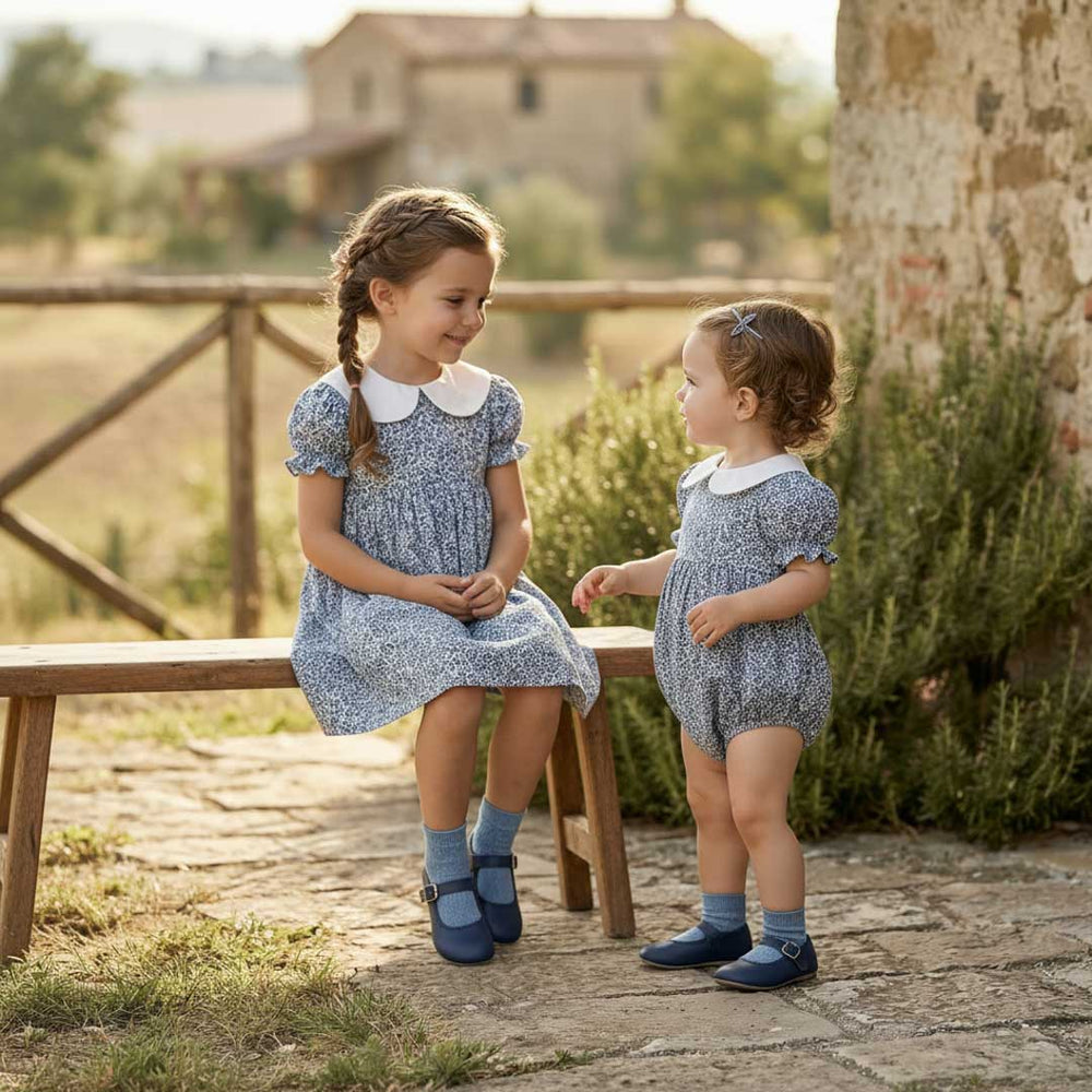 Two young girls in matching outfits sitting on a wooden bench outdoors.