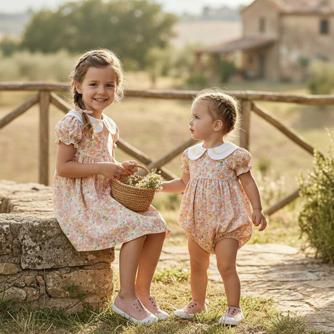 Two young girls in floral dresses standing outdoors with a rustic background