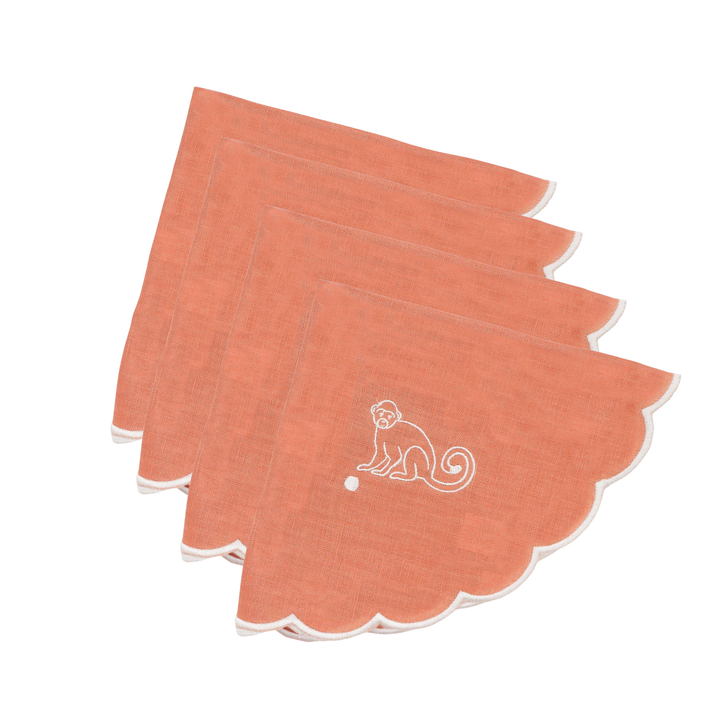 Four peach-colored square napkins with scalloped edges, stacked slightly offset. Each napkin features a white embroidered monkey design near the center, with a thin white border visible along the scalloped edge.