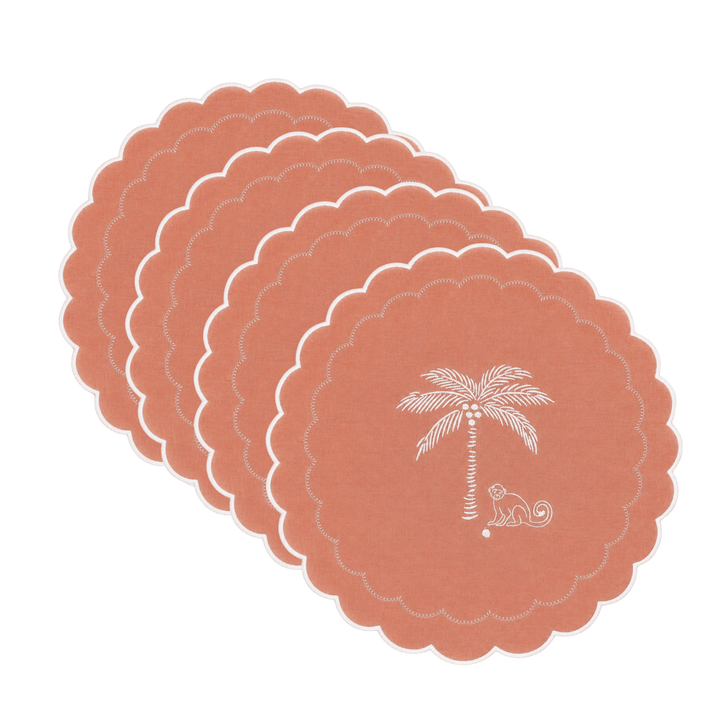 A set of 4 scalloped-edge round coasters in terracotta orange, fanned out on a white background. The front coaster features a white printed palm tree and coconut design with the text 'MILANOBORN'.