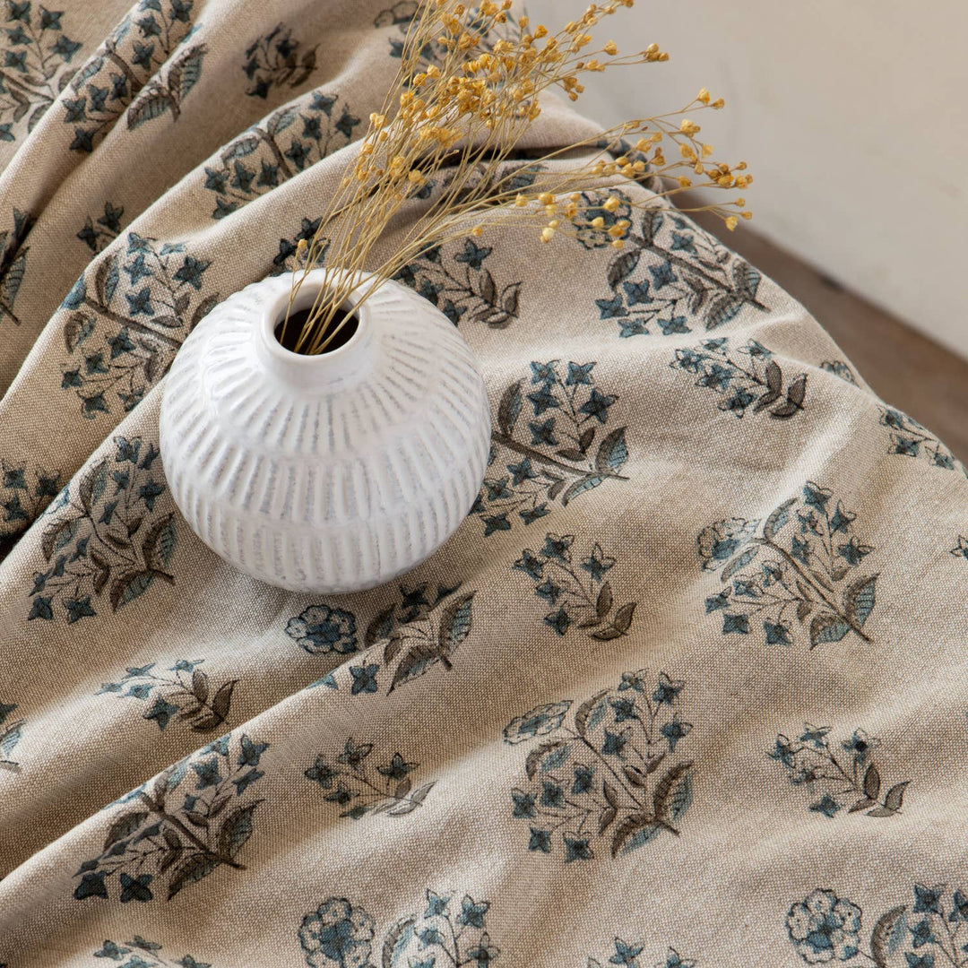 White vase with dried flowers on a beige fabric with floral patterns