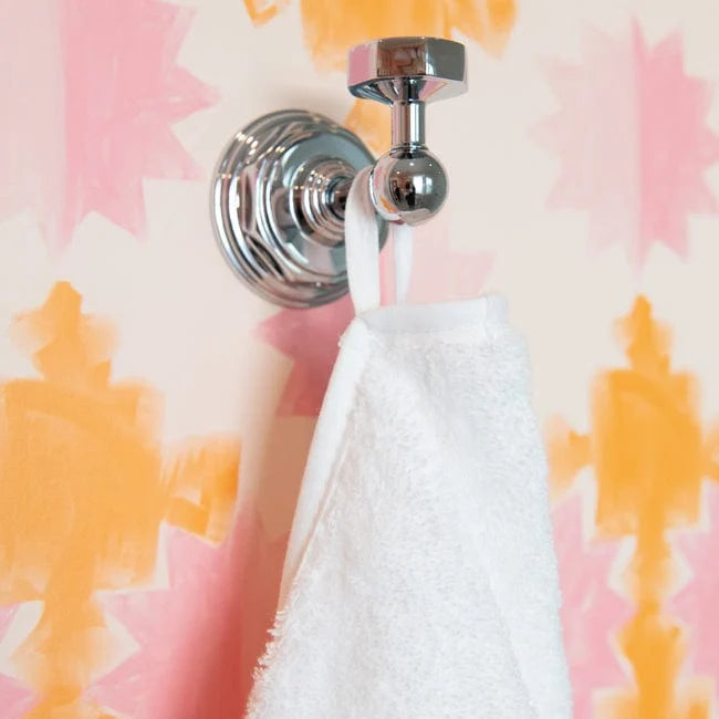 A polished chrome wall-mounted towel bar holding a white towel, set against a pink and orange abstract patterned wall.