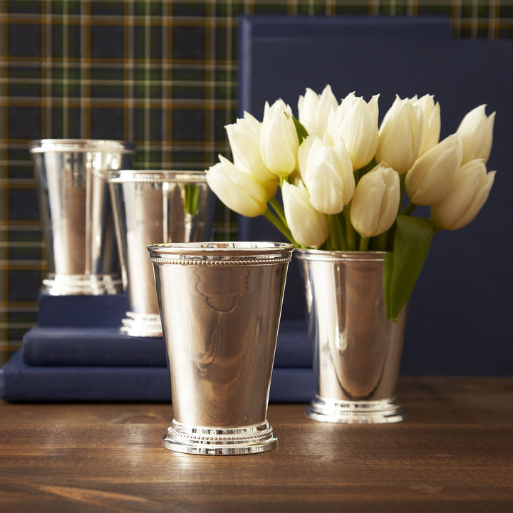 Silver mint julep cups with white tulips on a wooden surface against a plaid and blue background