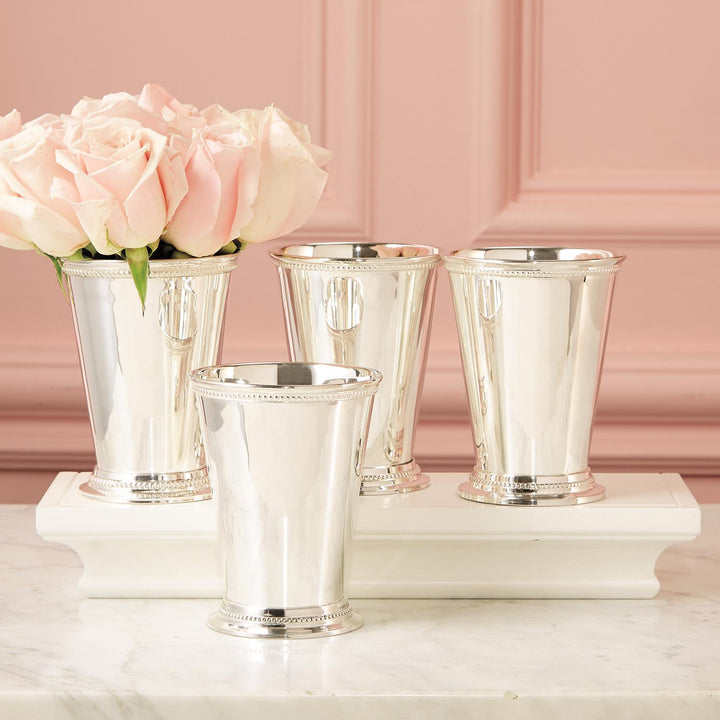 Silver mint julep cups with pink roses on a marble surface against a pink background
