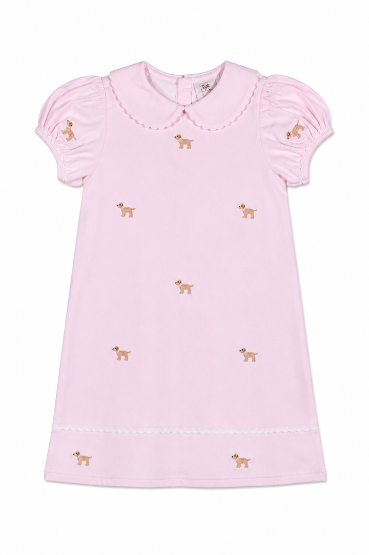 A light pink short-sleeve baby dress with a Peter Pan collar, scalloped trim, and embroidered dog motifs scattered across the front.