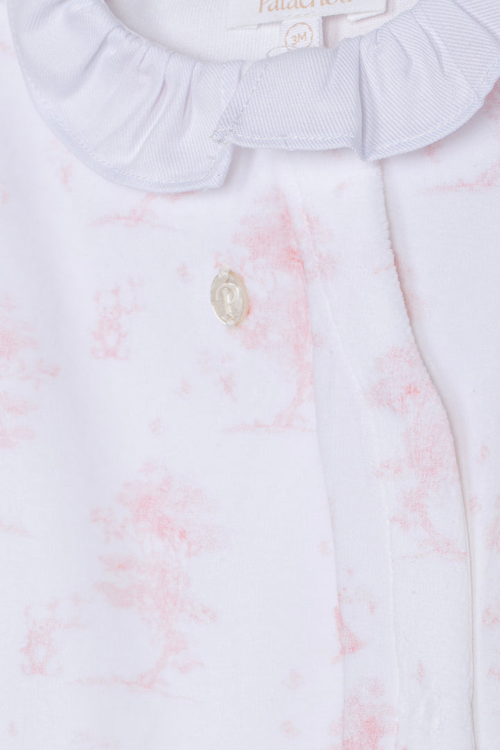 Close-up of a white baby garment with a soft pink floral pattern, featuring a ruffled collar and a small decorative button.