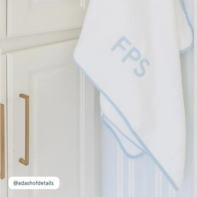 White towel with blue trim and 'FPS' monogram hanging on a white cabinet.