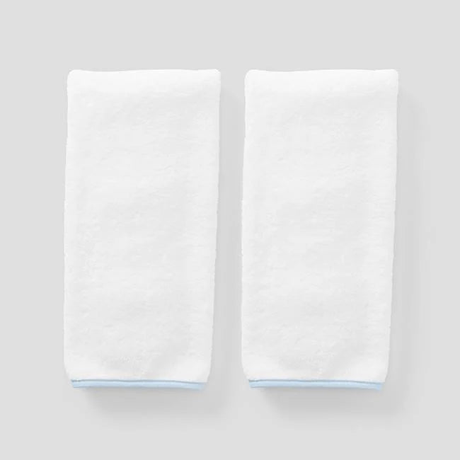Two folded white towels with light blue edges, displayed side-by-side on a neutral light gray background.