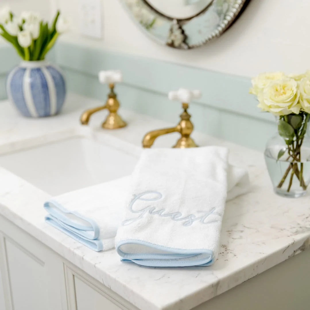 White towels with blue trim on a bathroom counter with flowers and a mirror.