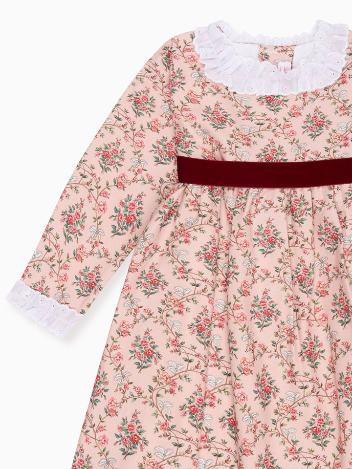 A long-sleeve baby dress with a light pink floral print, featuring a white ruffled collar, white ruffled cuffs, and a contrasting dark red velvet waistband.