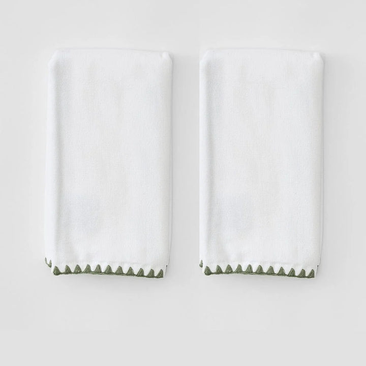 Two folded white towels with a green zigzag border along the bottom edge, displayed side by side on a light gray background.