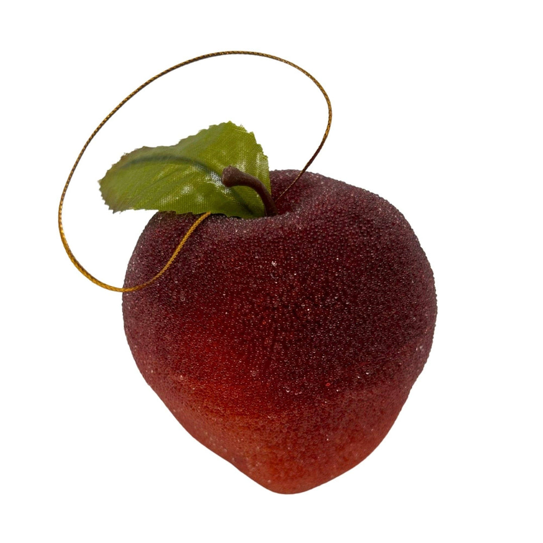 An artificial red peach decoration with a textured fuzzy surface, a green leaf, and a gold hanging loop, isolated on a white background.