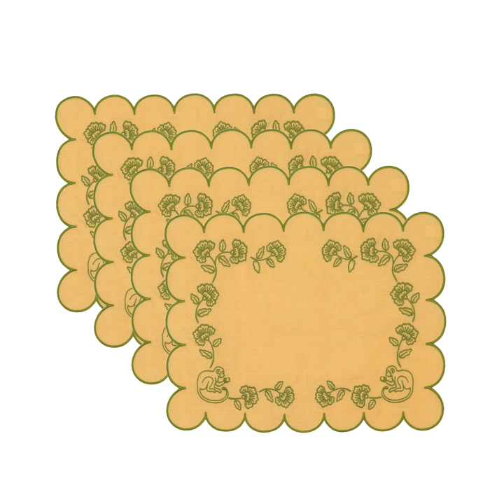 Four overlapping square placemats with scalloped edges and a green floral border pattern on a light yellow background, shown on a plain white background.