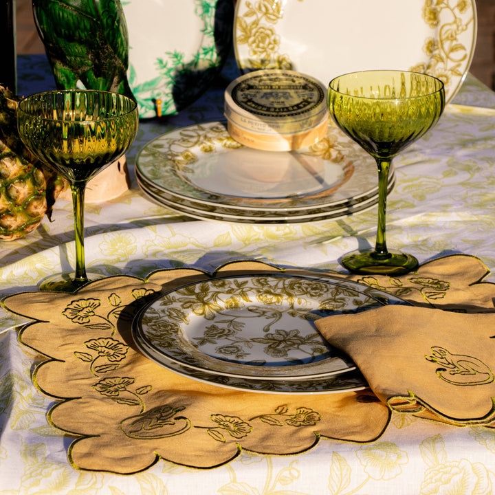 Decorative table setting with green glasses, plates, and embroidered napkins.