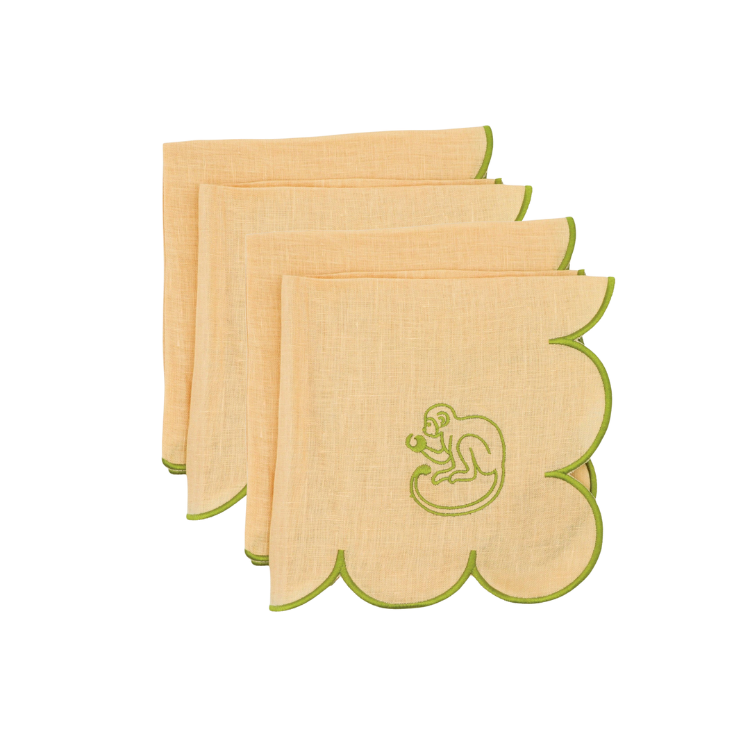 Four square linen napkins in a light peach-beige color with scalloped edges, featuring a green embroidered monkey motif on the front napkin.