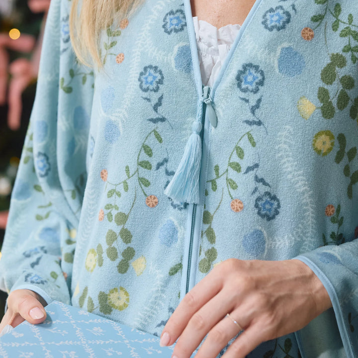 A close-up of a person wearing a light blue floral cardigan with tassel zipper details, holding a matching patterned item in one hand.