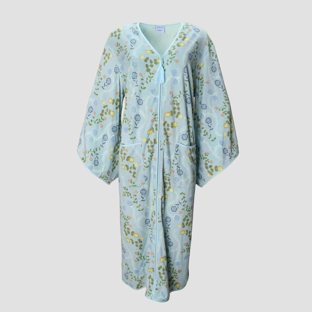 A light blue kaftan-style robe with a delicate floral and botanical print in green, yellow, and blue, featuring a V-neckline, front zipper, and side pockets, shown against a solid light gray background.