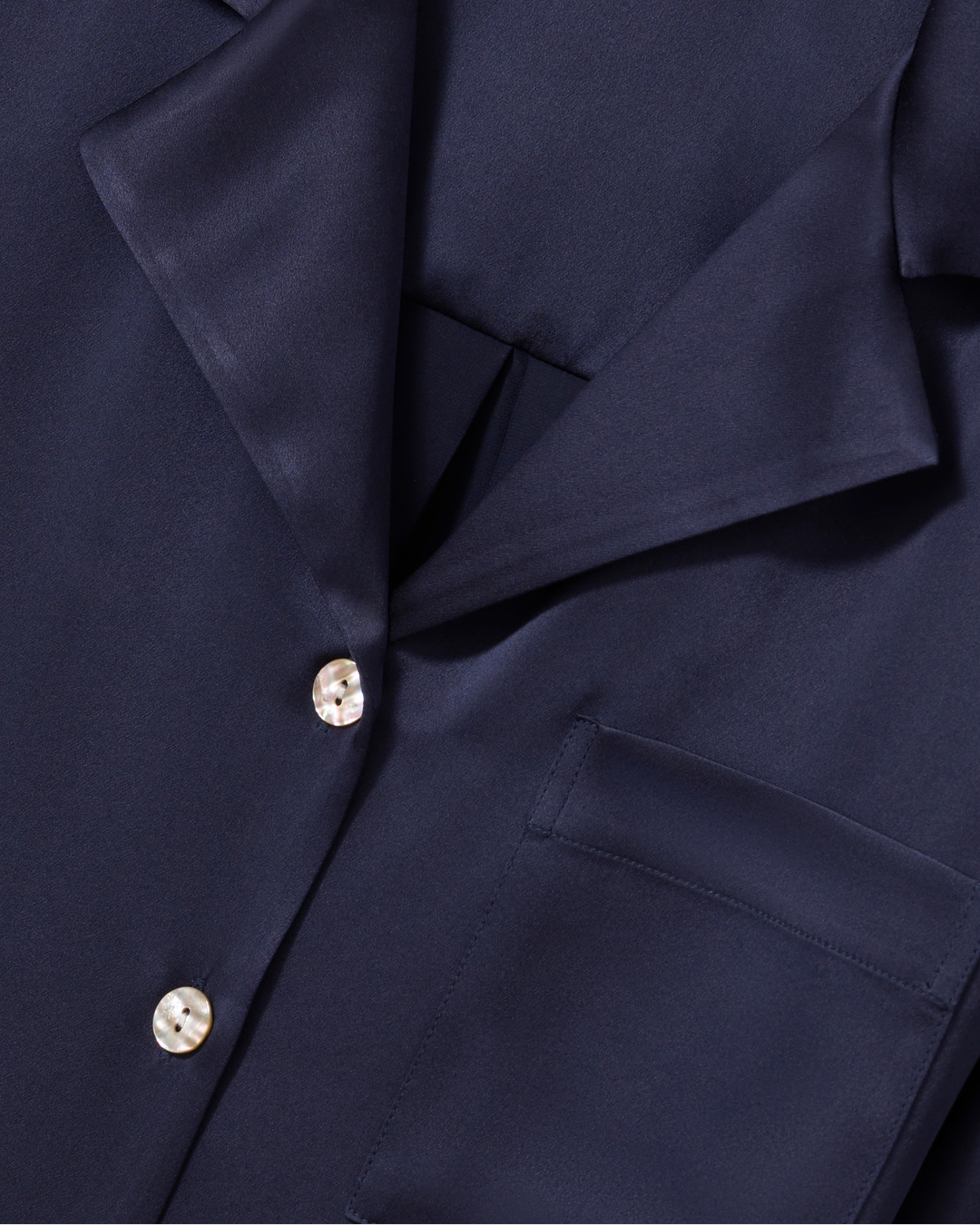 Close-up of a dark navy blue shirt or jacket fabric with a collar, front placket, and decorative pearl-like buttons.