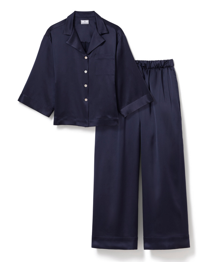 A two-piece pajama set in dark navy blue satin, featuring a short-sleeve button-front top with a collar and matching wide-leg pants, displayed on a clean white background.