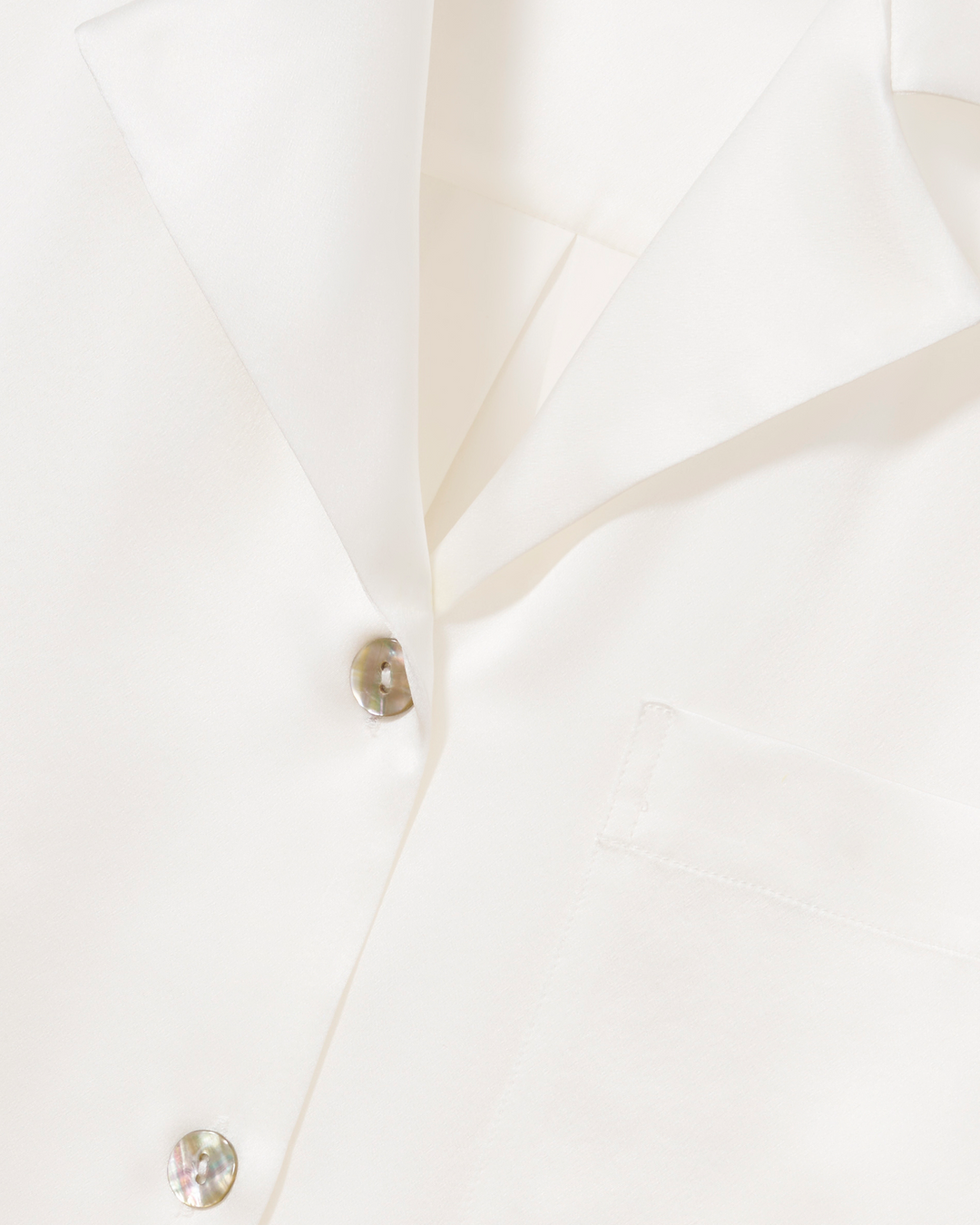 Close-up of a white collared shirt with iridescent round buttons and a white pocket.