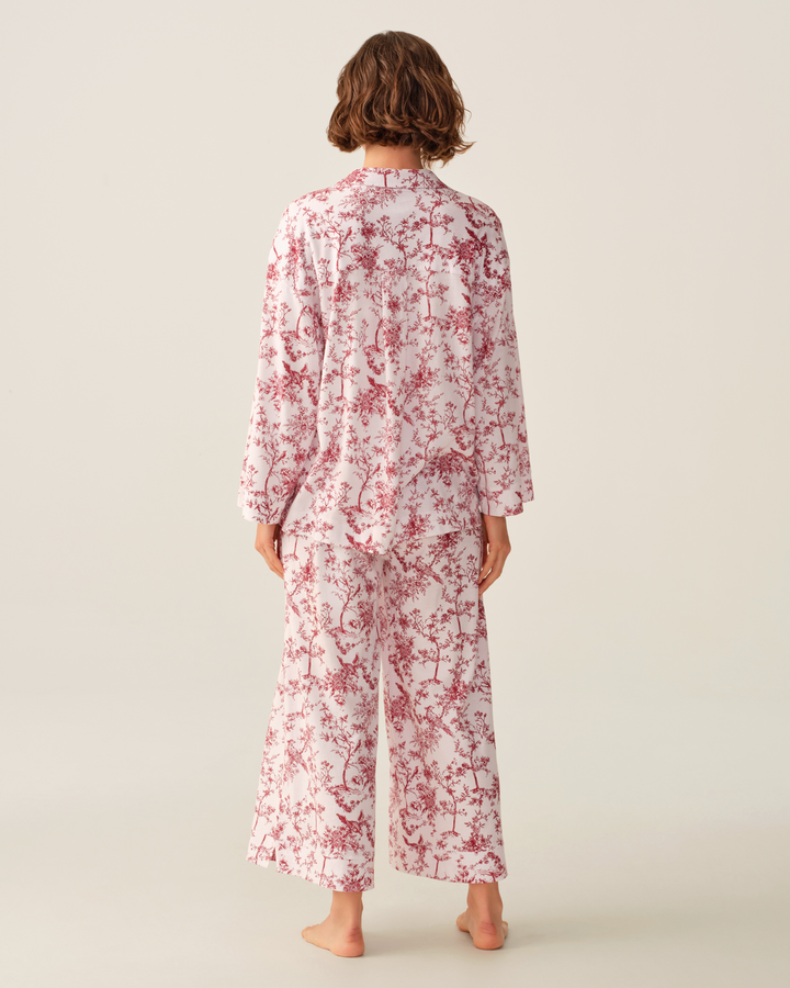 A model viewed from the back wearing a matching two-piece pajama set with a red floral print on a white background, set against a solid light beige studio backdrop.