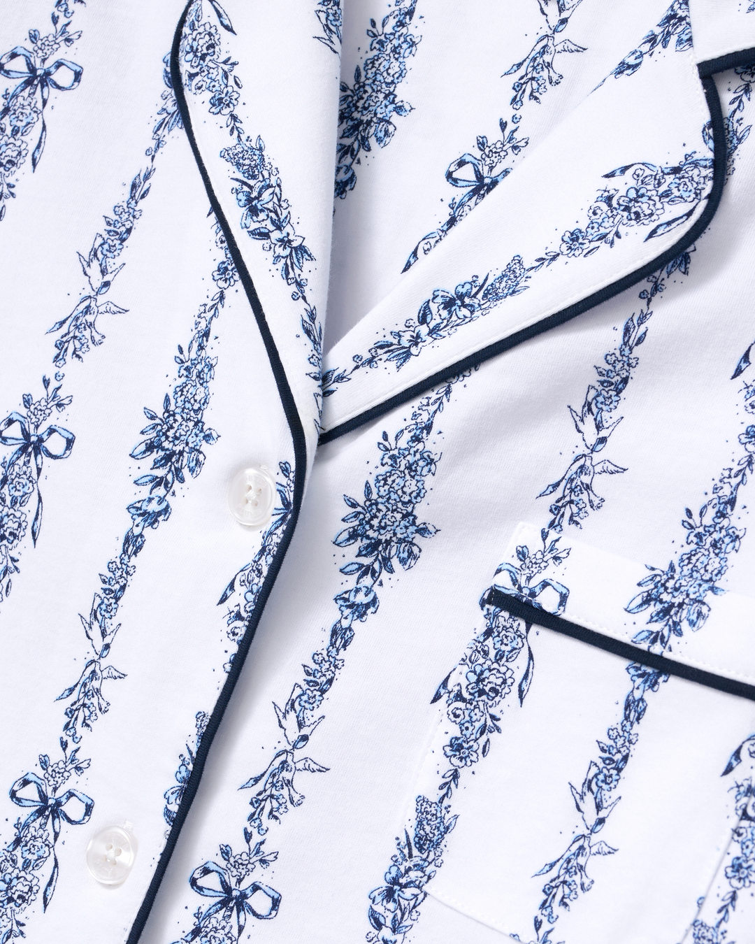 Close-up of a white pajama shirt with a blue floral toile pattern and black piping trim.