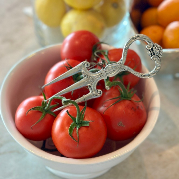 Decorative metal tool on a bowl of red tomatoes with lemons and oranges in the background.