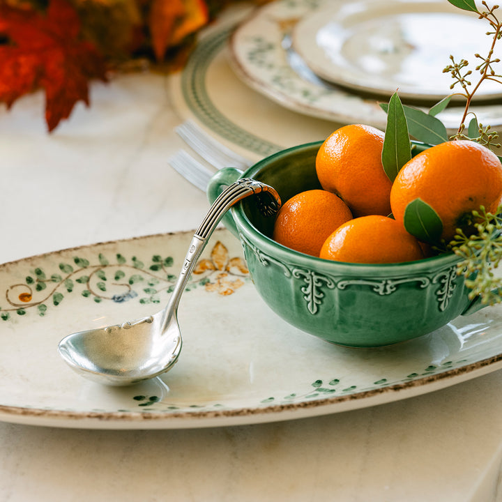 Bowl of oranges on a decorative table setting with a spoon and plates.