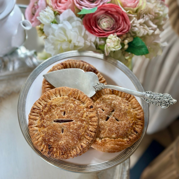 Three small pies on a silver platter with a decorative spoon, set against a floral background.