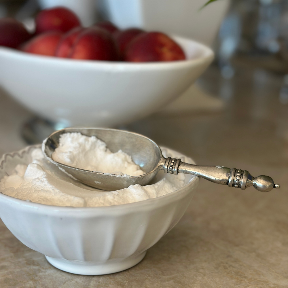 Silver scoop in a white bowl of sugar with peaches in the background