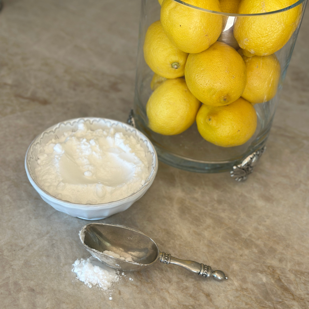 Bowl of powder sugar, silver scoop, and lemons on a stone surface