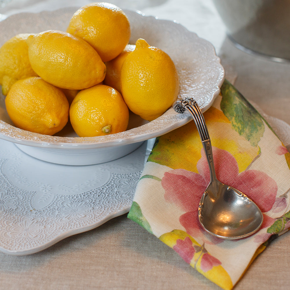 Bowl of lemons on a table with a floral napkin and spoon.