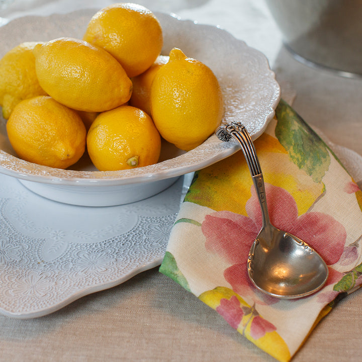 Bowl of lemons on a table with a floral napkin and spoon.