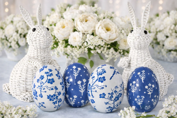 Decorative Easter eggs with floral patterns and woven bunny figures in front of white flowers.