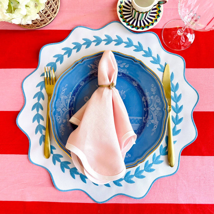 Table setting with blue plate, pink napkin, and gold cutlery on a red and white striped tablecloth.