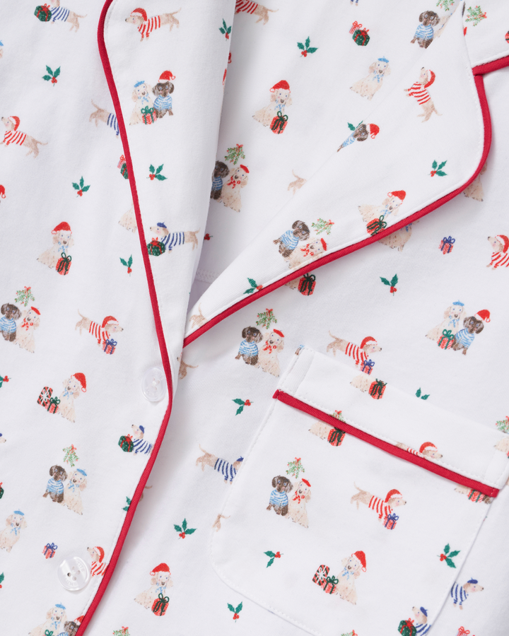 White pajama top with red piping and a festive print of dogs wearing Santa hats and holiday outfits, shown in a close-up flat lay.