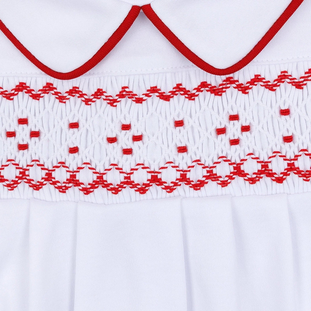 Close-up of a white garment with red embroidered trim and a smocked horizontal band across the chest.
