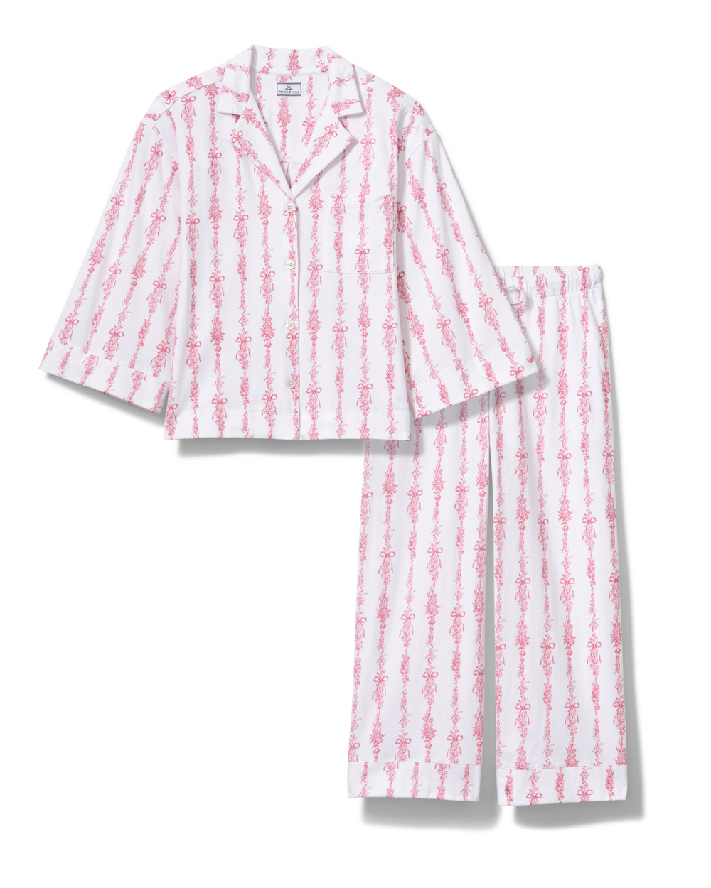 A two-piece pajama set featuring a short-sleeve button-front top and matching pants, both in a white fabric with a vertical pink pattern of stylized figures, shown on a plain white background.