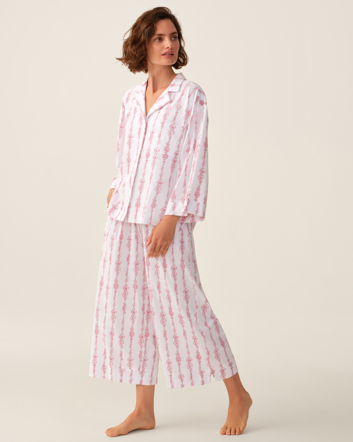 A woman modeling a two-piece pajama set with a white base and pink vertical striped pattern, photographed against a plain light beige studio background.