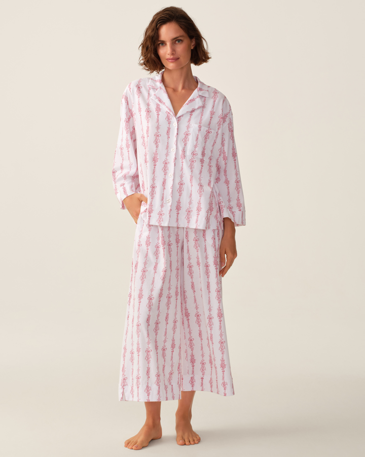 A woman modeling a matching two-piece pajama set with a white base and pink vertical striped pattern, standing against a plain light beige studio background.