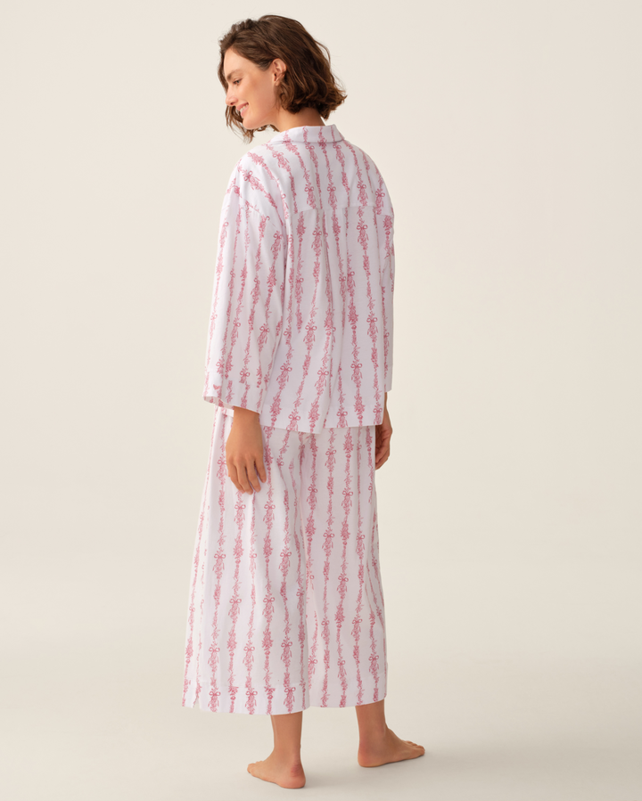 A woman wearing a matching two-piece pajama set with vertical pink and white stripes, shown from the back against a plain beige studio background.